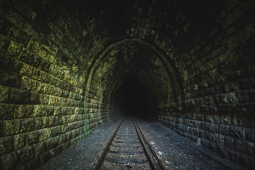 old, dark, abandoned tunnel with railroad track