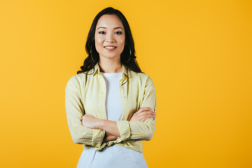 smiling asian girl with crossed arms isolated on yellow