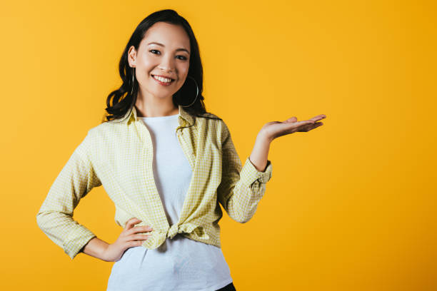 istock smiling asian girl presenting something isolated on yellow 1162092073