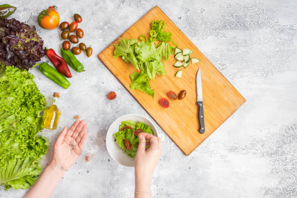 Woman adding salt in vegetable salad bowl. Health eating concept.