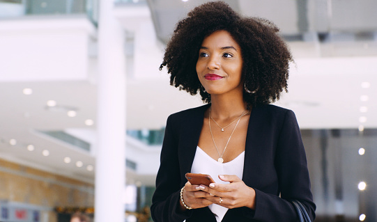 Shot of a young businesswoman using a smartphone while walking through a modern office