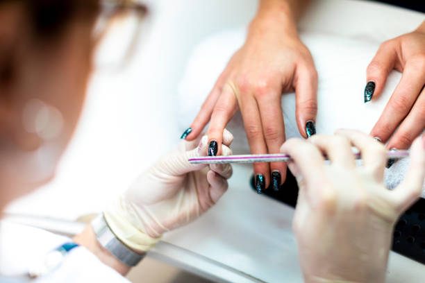 Manicurist using a file on a fingernail to remove excess cuticles and prepare it for painting A nail file being used to tidy up a nail and remove cuticles during a manicure procedure. Nail Art stock pictures, royalty-free photos & images