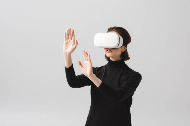 brunette young woman wearing virtual reality headset while gesturing isolated on grey stock photo