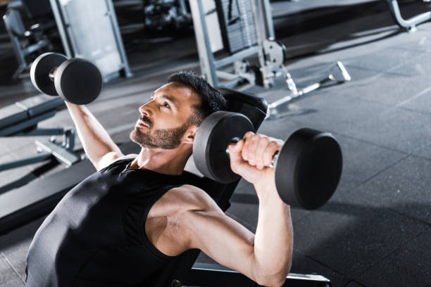 istock selective focus of handsome strong man working out with dumbbells in gym 1162094467