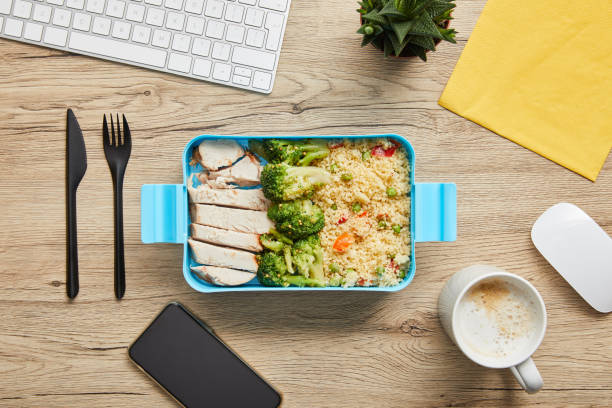 istock Top view of lunch box with chicken, broccoli and risotto on table with computer keyboard and smartphone 1162094740