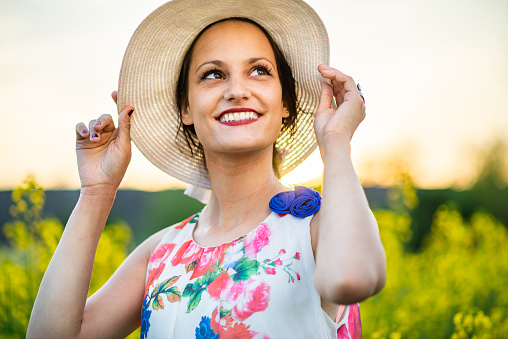 Beautiful women with hat between yellow flowers on a sunset.