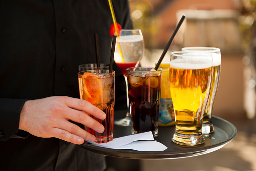 Cropped out photo of waiter in black uniform serving drinks on the tray, selective focus, people in the background out of focus