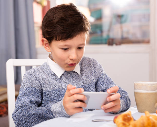 istock Boy looking to smartphone screen at the table in the kitchen 1162103117