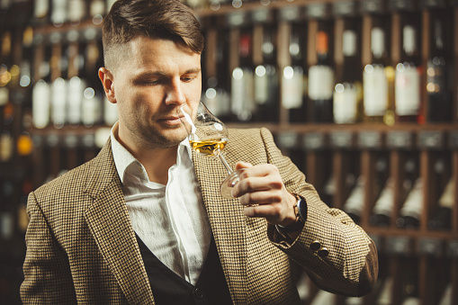 Close-up shot of young sommelier smell whiskey on cellar background. Expert in the field of alcoholic beverages.
