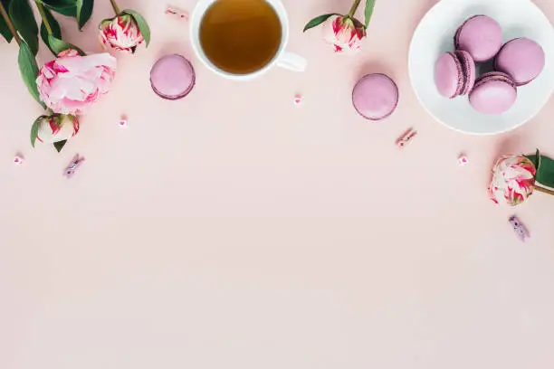 Photo of Top view of macaroons with a Cup of tea and peonies.