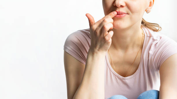 red bubbles of virus herpes on lips of a woman in light pink t-shirt, lower part face is seen, which she touches with her finger. medicine, treatment. horizontal with copy space. white background - lubrication infection imagens e fotografias de stock