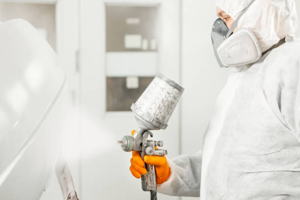 istock Car painter spraying white paint with spray gun on vehicle in paint chamber. 1162107036