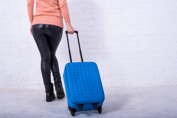istock A woman with a blue suitcase near a white brick wall, copy space. 1162108149
