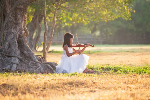 Photo of An Asian girl wearing a white dress is playing a violin