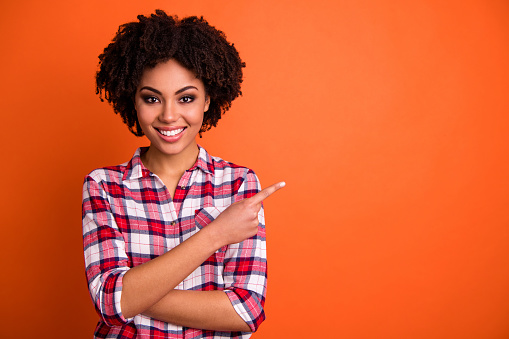 Close-up portrait of her she nice attractive cheerful cheery confident, wavy-haired lady wearing checked shirt pointing aside tips feedback advert isolated on bright vivid shine orange background