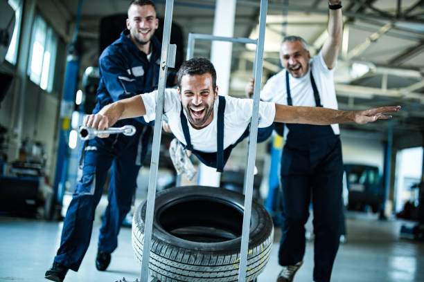 Cheerful auto mechanic having fun with his colleagues in a workshop and looking at camera.
