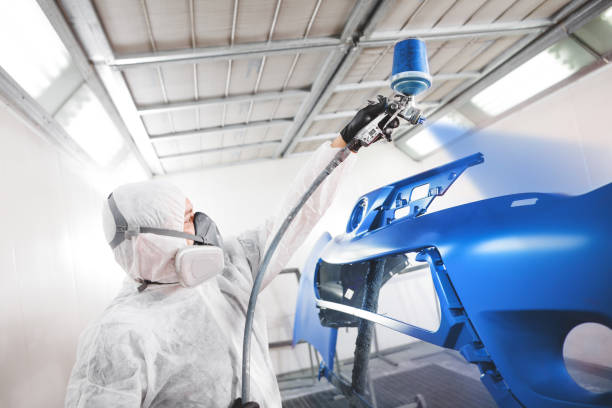 istock Male worker in protective clothes and mask painting car bumper using spray paint. 1162110426