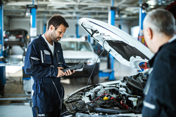 Auto mechanic working with car diagnostic tool in a repair shop. Young mechanic analyzing car's performance with diagnostic tool in a workshop. auto repair shop stock pictures, royalty-free photos & images