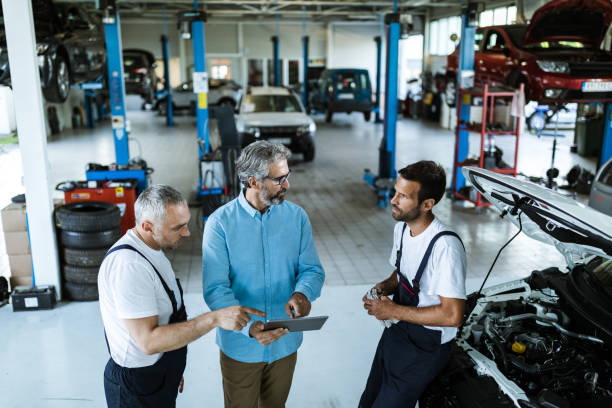 gerente de adultos medio usando touchpad y hablando con mecánicos de coches en un taller. - customer auto repair shop car mechanic fotografías e imágenes de stock