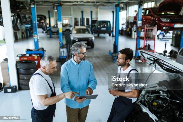 Mid Adult Manager Using Touchpad And Talking To Car Mechanics In A Workshop Stock Photo - Download Image Now