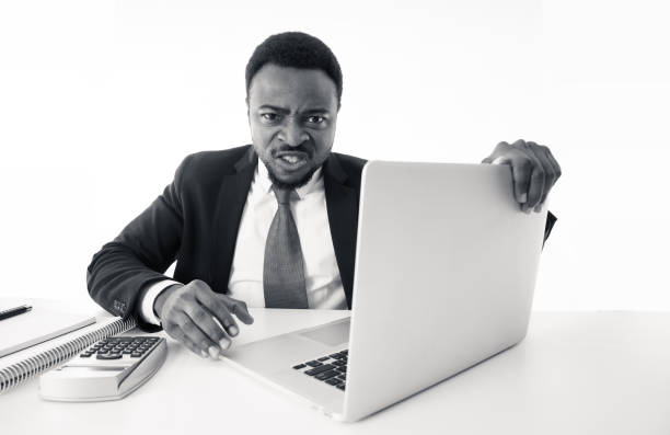 istock Angry and desperate african american entrepreneur businessman shouting at computer feeling tired and overworked at desk in People, Stress, Technology and Overtime concept isolated in white background. 1162116062