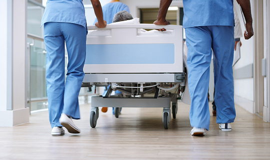 Closeup shot of a group of medical practitioners pushing a patient down a hospital corridor in a gurney