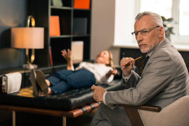 잘 생긴 심각한 회색 머리 정신과 의사 앉아 에 그의 사무실 - psychiatrists couch 뉴스 사진 이미지