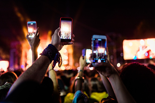 Unrecognizable crowd filming music festival through their cell phone by night.