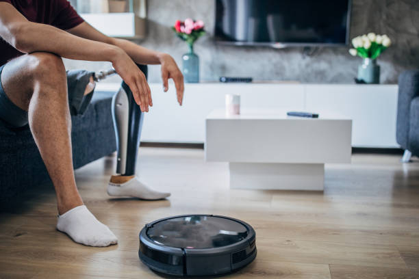 istock Man with one leg sitting next to robot vacuum cleaner 1162124145