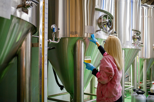 Female master brewer inspecting beer from fermenting tank