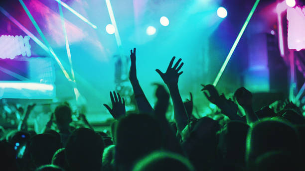 Cheering crowd at a concert. Rear view of excited crowd enjoying a concert performance of a unrecognizable artist. Raised hands of fans are in the focus against green and purple lit stage. clubbing stock pictures, royalty-free photos & images