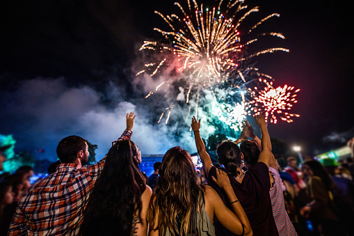 Back view of large group of people watching fireworks on the sky by night.