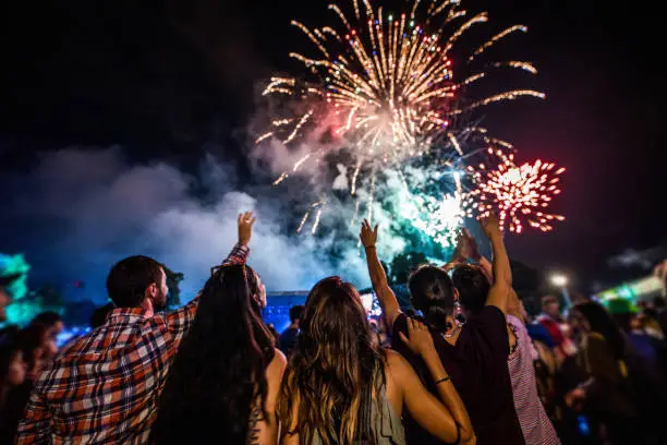 Photo of Rear view of crowd of people watching fireworks at night.