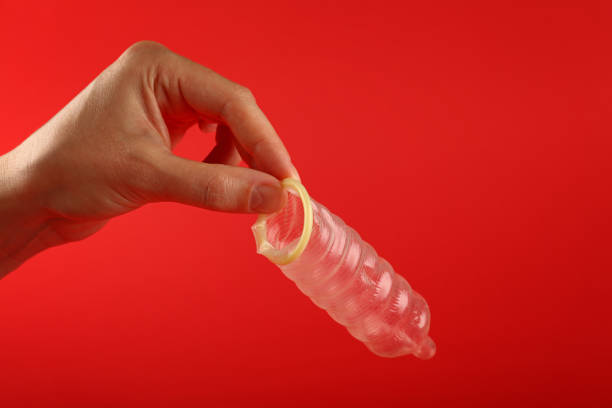 istock Close up man hand holding open condom over red 1162125970
