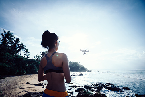Woman flying drone which taking photo over sea