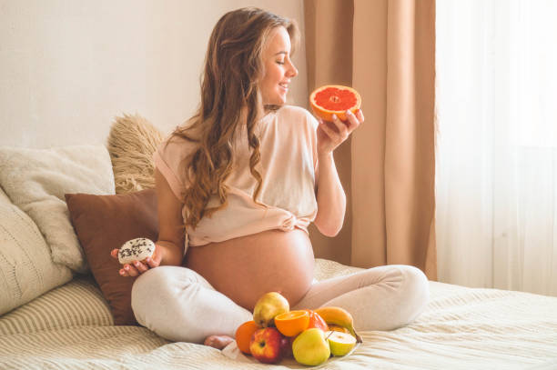 妊娠と健康的な有機栄養。妊娠と食べ物の選択。ベッドで新鮮な果物を楽しむ妊娠中の女性、フリースペース - freshness human hand mother family ストックフォトと画像