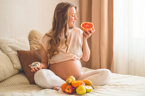 Pregnancy and healthy organic nutrition. Pregnancy and food choice. Pregnant woman enjoying fresh fruits in bed, free space