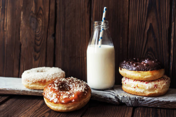 kilka pączków i mleka w butelce ze słomką na ciemnym drewnianym, teksturowanym rustykalnym tle - cream sprinkles food and drink freshness zdjęcia i obrazy z banku zdjęć