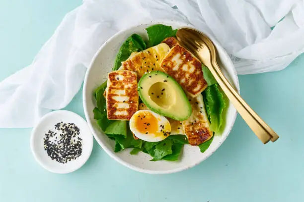 keto ketogenic diet soft boiled eggs with grilled haloumi, avocado and lettuce, mediterranean cuisine on pastel background