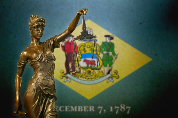 Close-up of a small bronze statuette of Lady Justice before a flag of Delaware.