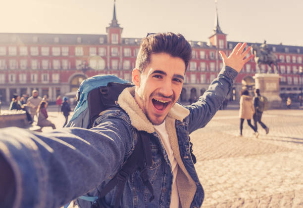 istock Attractive young tourist student man with backpack having fun excited taking a happy face selfie with smart phone in Plaza Mayor, Madrid, Spain. Vacation, and travel around the world concept. 1162141065