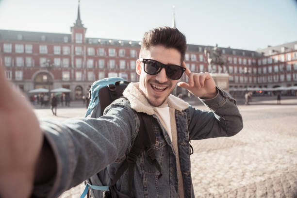 istock Attractive young tourist student man with backpack having fun happy and excited taking a funny face selfie with smart phone in Plaza Mayor, Madrid, Spain. Vacation, and travel around the world concept. 1162141251
