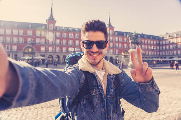 istock Attractive young tourist student man with backpack having fun happy and excited taking a funny face selfie with smart phone in Plaza Mayor, Madrid, Spain. Vacation, and travel around the world concept. 1162141256