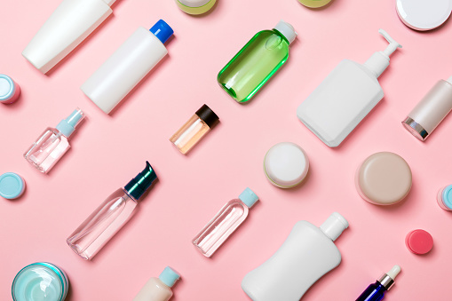 Top view of different cosmetic bottles and container for cosmetics on pink background. Flat lay composition with copy space.