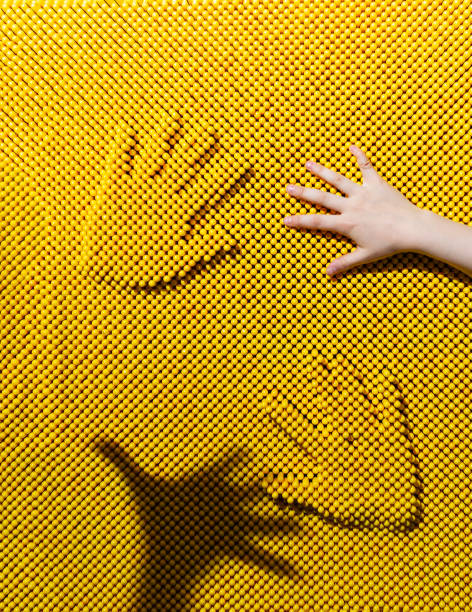 Two handprints on the yellow plastic pinscreen, children's hand and hand shadow