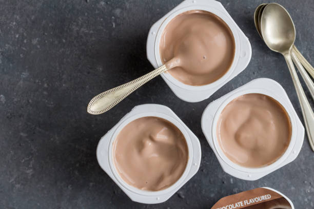 Yogurt cups with chocolate flavoured yoghurt on dark grey background with spoons - top view photo