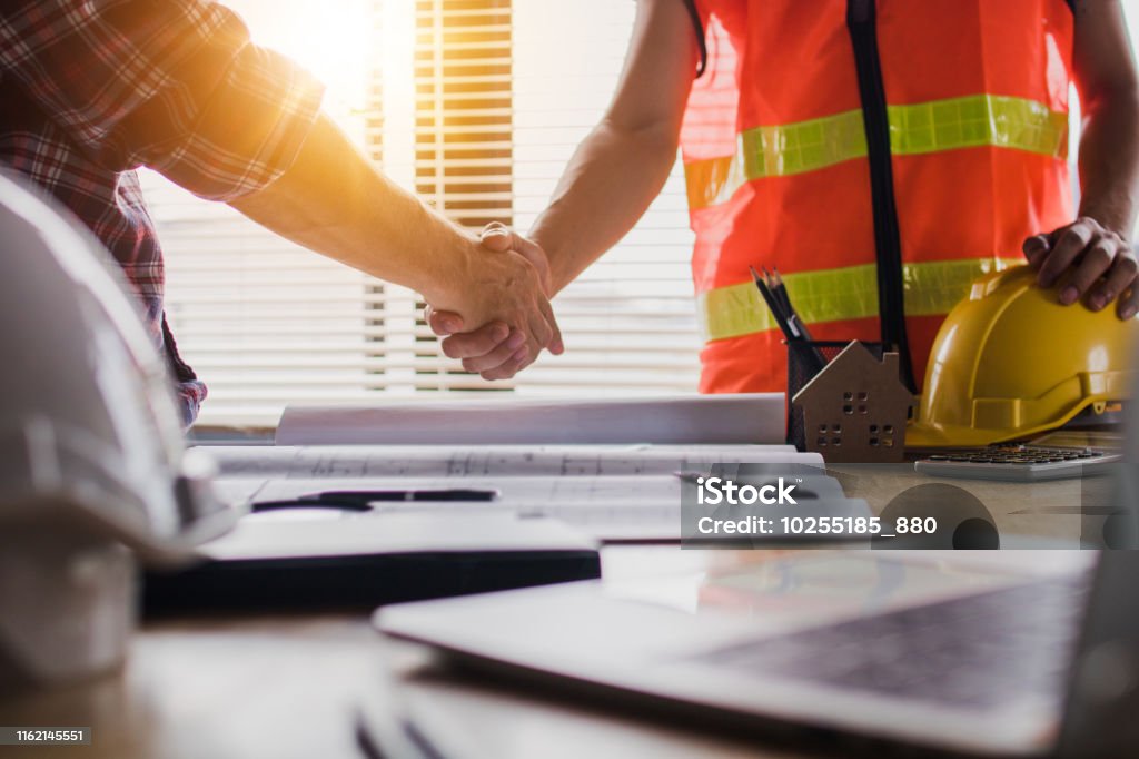 Apretón de manos de dos hombres de negocios, después de arquitecto trabajando y planificando el plan, objetos de ingeniería en el lugar de trabajo - Foto de stock de Sector de la construcción libre de derechos