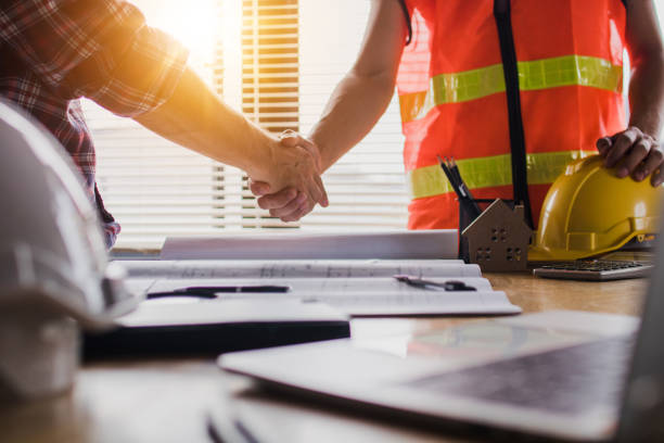 apretón de manos de dos hombres de negocios, después de arquitecto trabajando y planificando el plan, objetos de ingeniería en el lugar de trabajo - engineer architect building contractor team fotografías e imágenes de stock