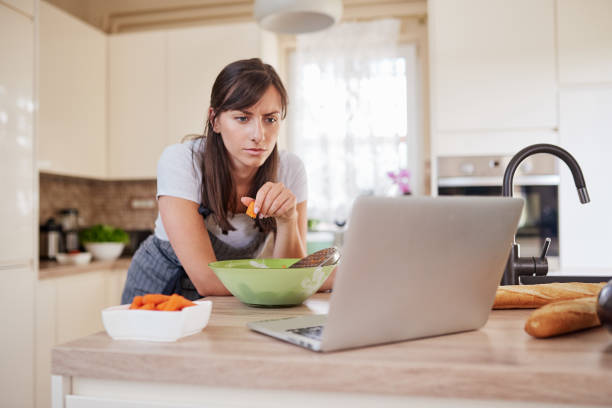 istock Woman looking at recipe on laptop while standing in kitchen. 1162147181