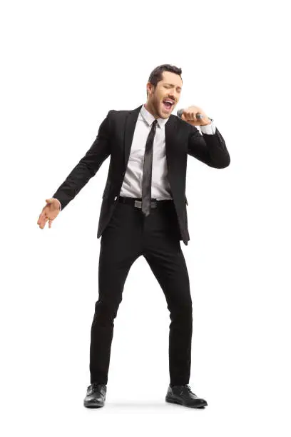 Full length portrait of a young man in a suit singing on a mic isolated on white background